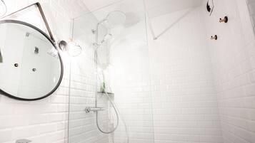 Un bagno moderno con pareti piastrellate di bianco, uno specchio rotondo, una cabina doccia in vetro e un lavandino bianco.