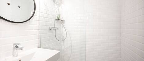 Un baño con lavamanos blanco, espejo y ducha.