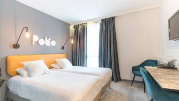 Habitación de hotel con dos camas, un escritorio, una silla, un televisor y un ventanal con cortinas.