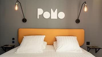 A neatly made bed with white linens and two pillows, a headboard in a warm orange color, and a wall-mounted sign with the word "Pomo".