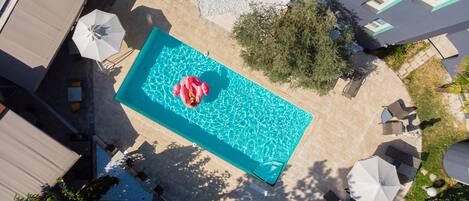 An aerial view of a swimming pool with a pink flamingo float, surrounded by outdoor seating and a garden area.