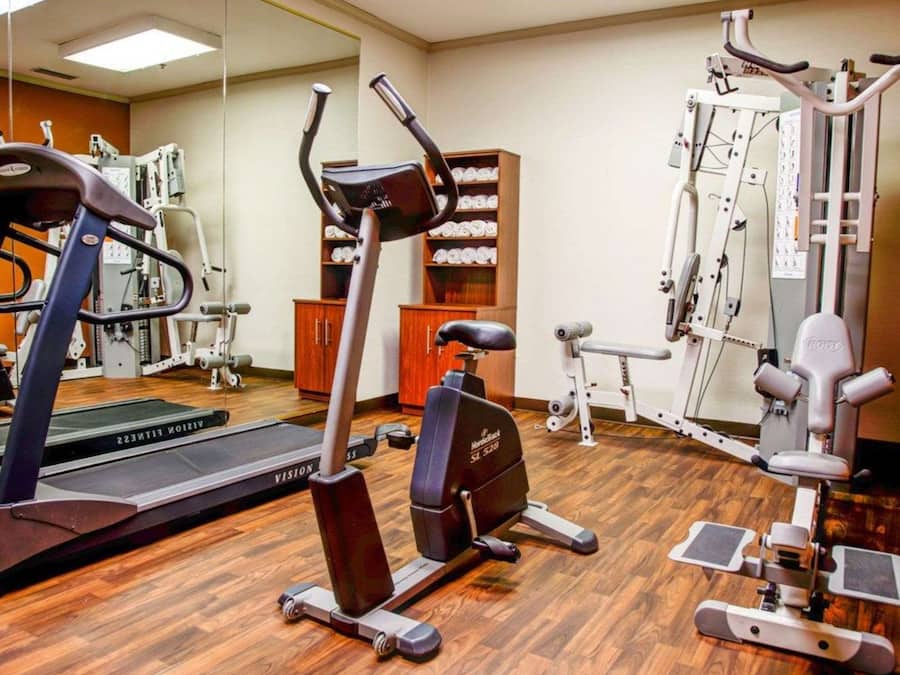 A gym with cardio machines, weight training equipment, and a mirrored wall.