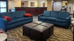 A hotel lobby with two blue sofas, a brown ottoman, a reception desk, and a coffee station. - Comfort Suites Gadsden Attalla (Attalla)