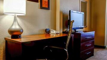 A hotel room with a desk, a lamp, a chair, a television, and a telephone.