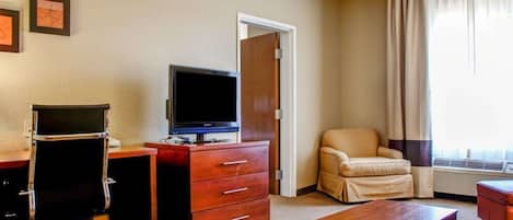 Une chambre d’hôtel équipée d’un bureau, d’une télévision, d’une chaise, d’une petite table et d’une porte donnant sur une autre pièce.