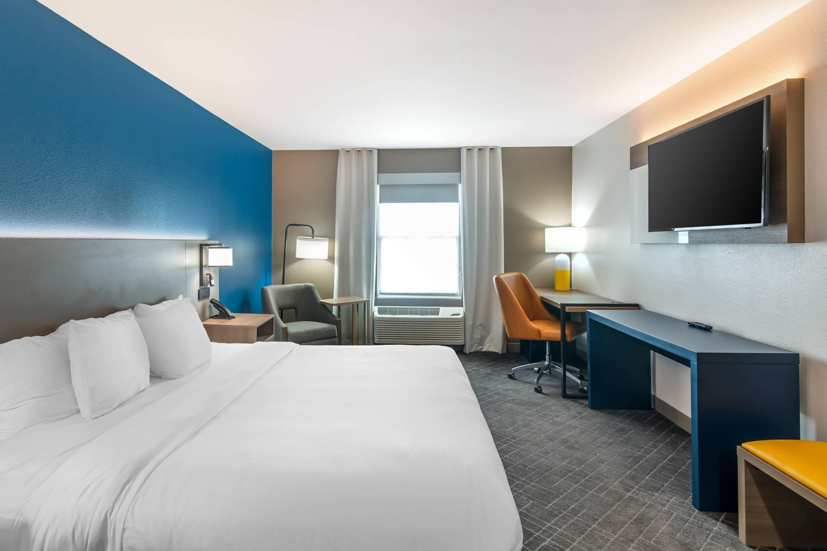 A hotel room with a large bed, a desk, a chair, a TV, and a window with curtains.