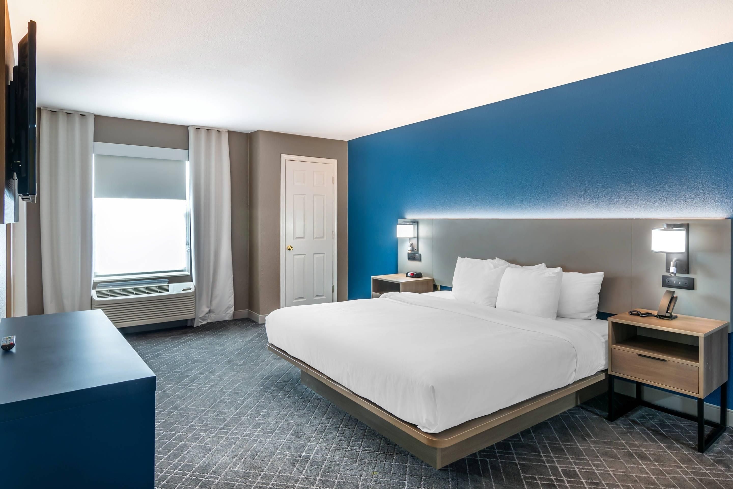 A hotel room with a bed, bedside tables, a desk, a TV, and a window with curtains.