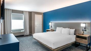 A hotel room with a bed, bedside tables, a desk, a TV, and a window with curtains.