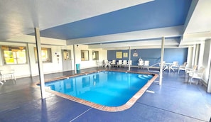 An indoor swimming pool with a blue interior, surrounded by white chairs and tables, and a blue ceiling. - Comfort Inn & Suites Chesterfield - St. Louis (Chesterfield)