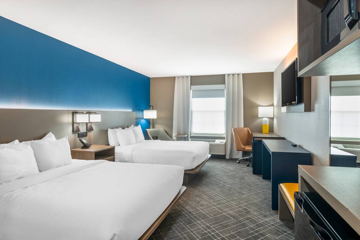 A hotel room with two beds, a desk, a chair, a TV, and a large window.