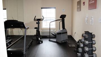 A gym with a treadmill, elliptical, stationary bike, and a rack of dumbbells.