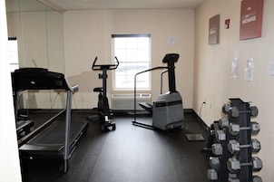 A gym with a treadmill, elliptical, stationary bike, and a rack of dumbbells.