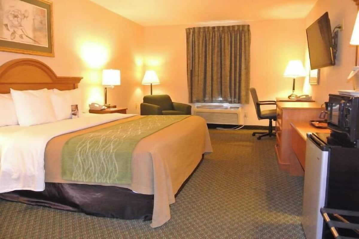 A hotel room with a bed, desk, chair, television, and air conditioning unit.