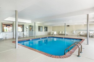 Una piscina interior con agua azul cristalina, rodeada de sillas y mesas blancas y un suelo de baldosas.