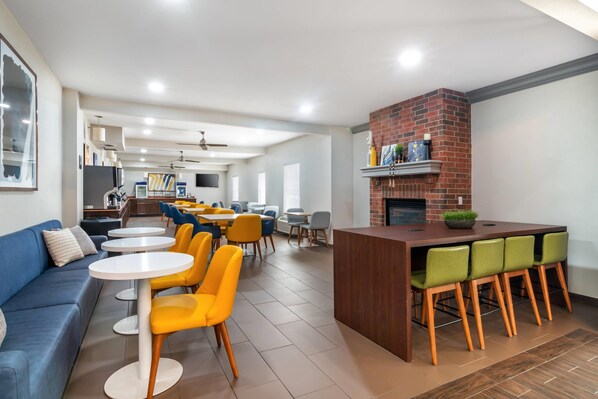 A modern dining area with a brick fireplace, yellow and blue chairs, and a blue sofa. - Comfort Inn & Suites Chesterfield - St. Louis (Chesterfield)