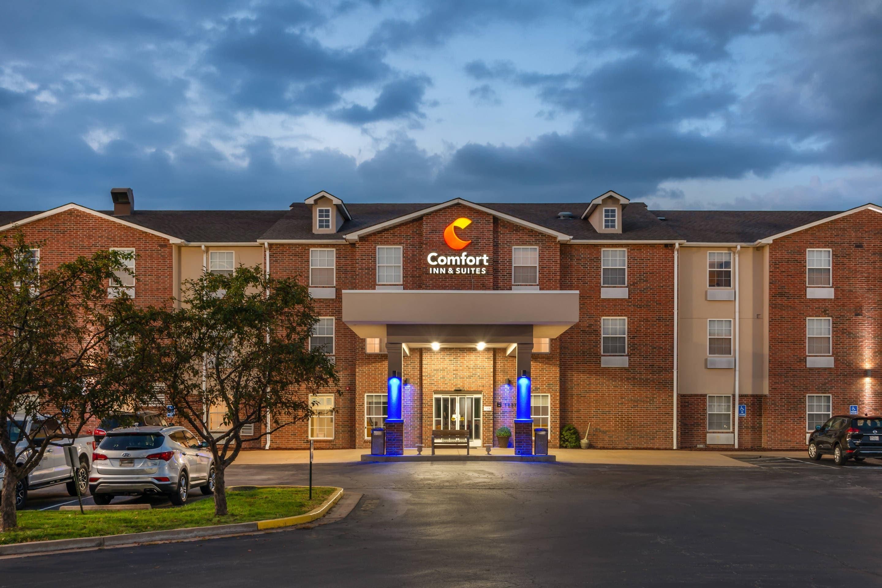 Un Comfort Inn & Suites con fachada de ladrillo, una entrada central y un estacionamiento con coches.
