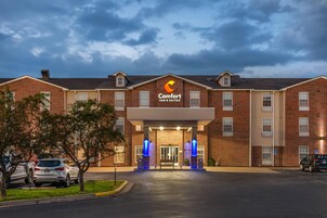Un Comfort Inn & Suites con fachada de ladrillo, una entrada central y un estacionamiento con coches.