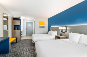 A hotel room with two beds, a desk, a mirror, and a wardrobe.