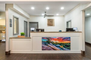 Una recepción con un letrero que dice '¡Bienvenido!', un cuadro de un paisaje y un horario de registro de entrada y salida en la pared.