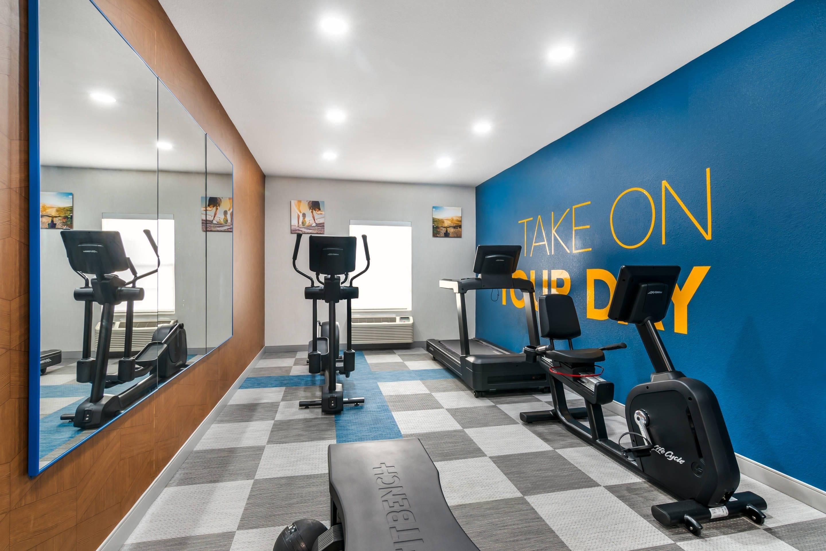 A gym with exercise equipment, a blue wall with motivational text, and a checkered floor.