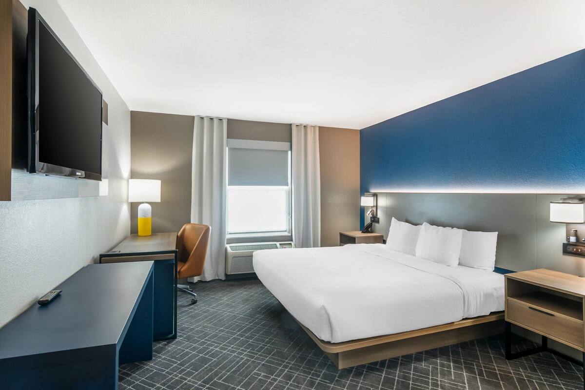 A hotel room with a bed, desk, chair, TV, and a window with curtains.