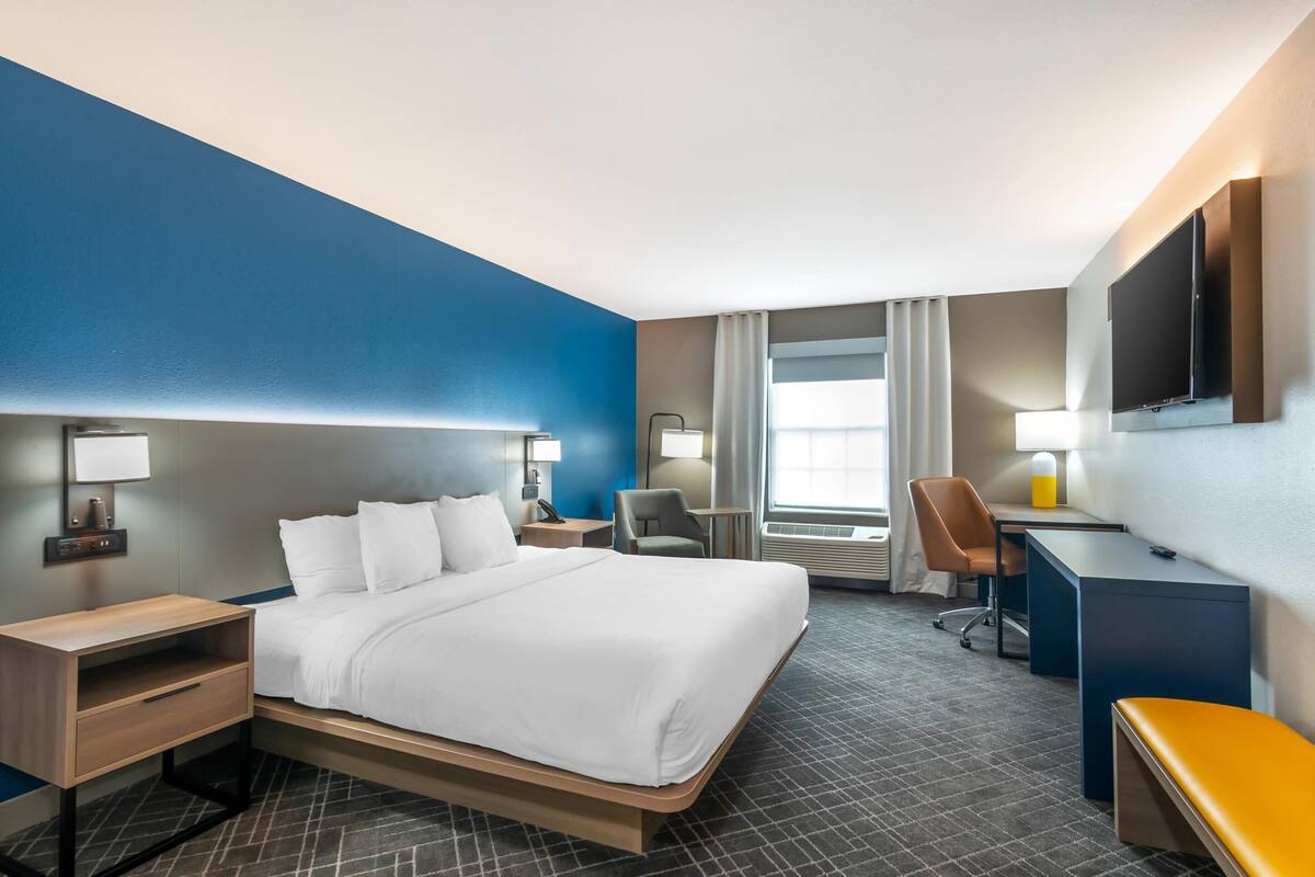 A hotel room with a bed, desk, chair, and TV.