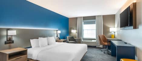 A hotel room with a bed, desk, chair, and TV.