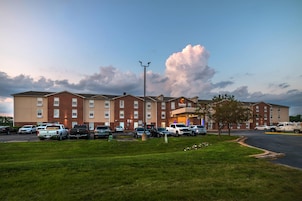Un hotel con fachada de ladrillo, varios espacios de estacionamiento y una zona verde al frente.
