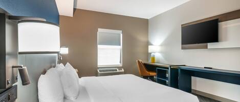 A hotel room with a bed, desk, chair, television, and a window.