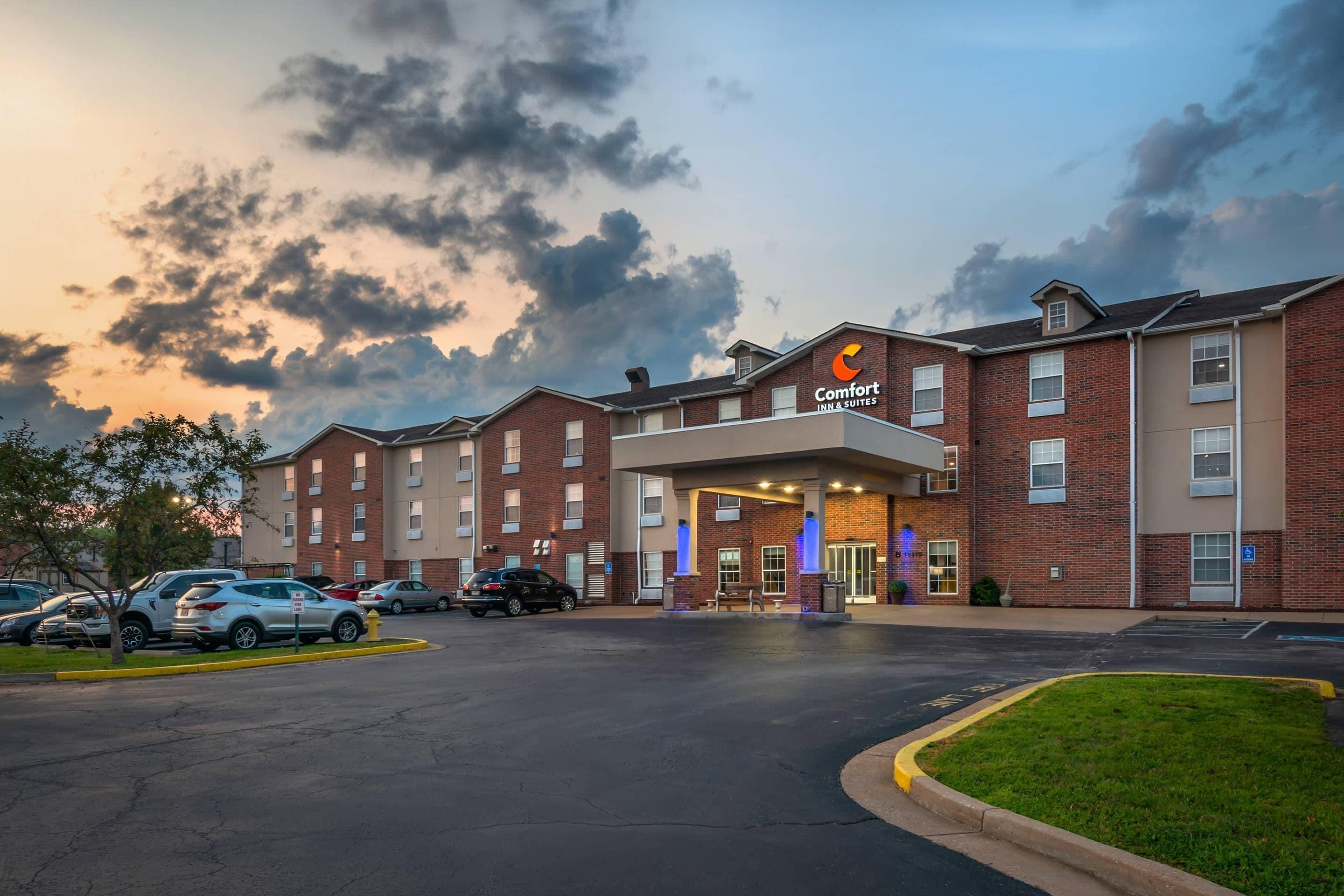 Un hotel Comfort Inn & Suites con fachada de ladrillo, múltiples ventanas y un estacionamiento con varios automóviles.
