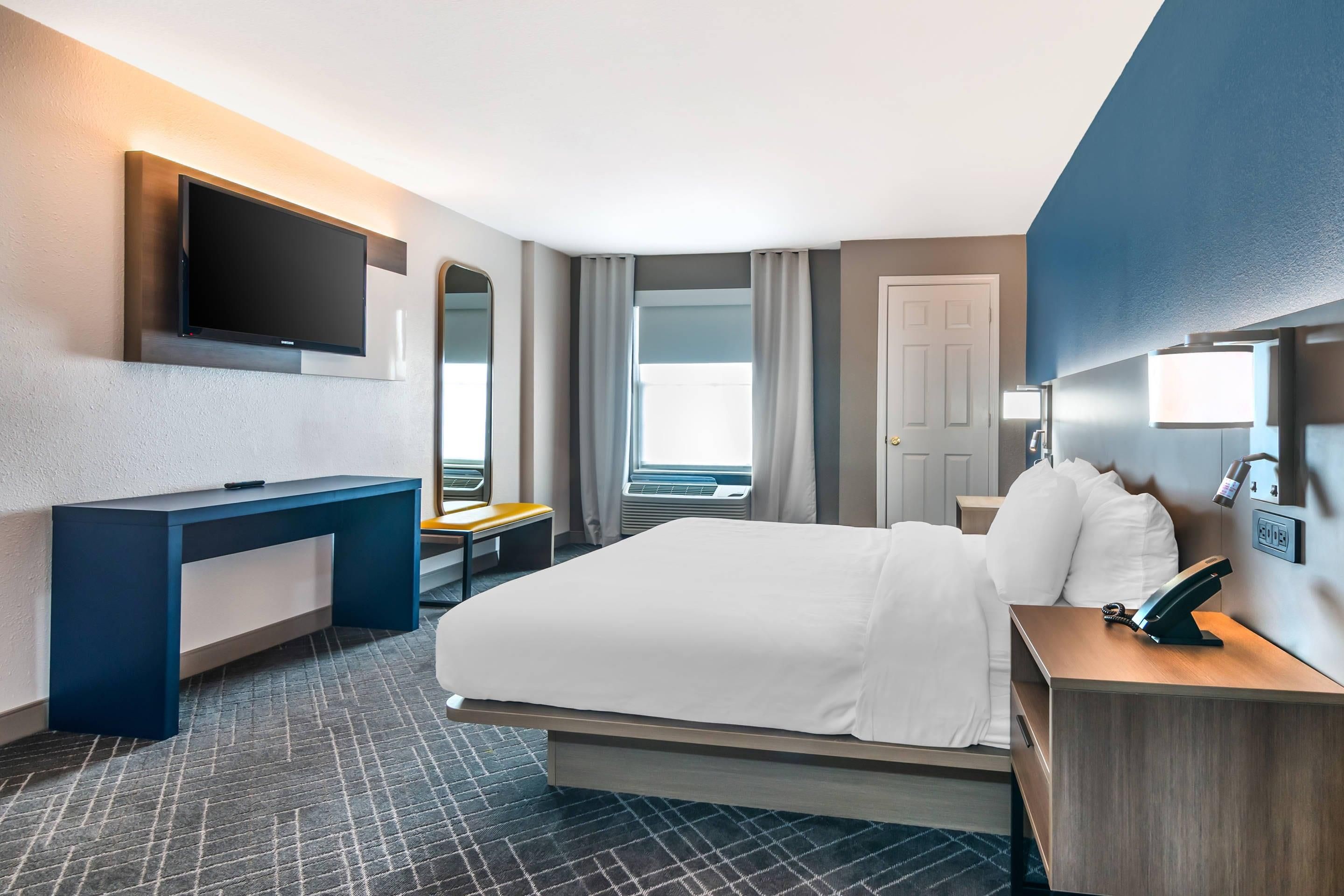 A hotel room with a bed, desk, chair, television, and a window with curtains.