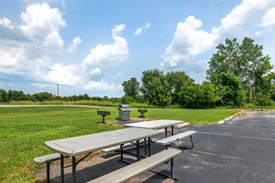 A picnic area with tables and benches, surrounded by grass and trees.