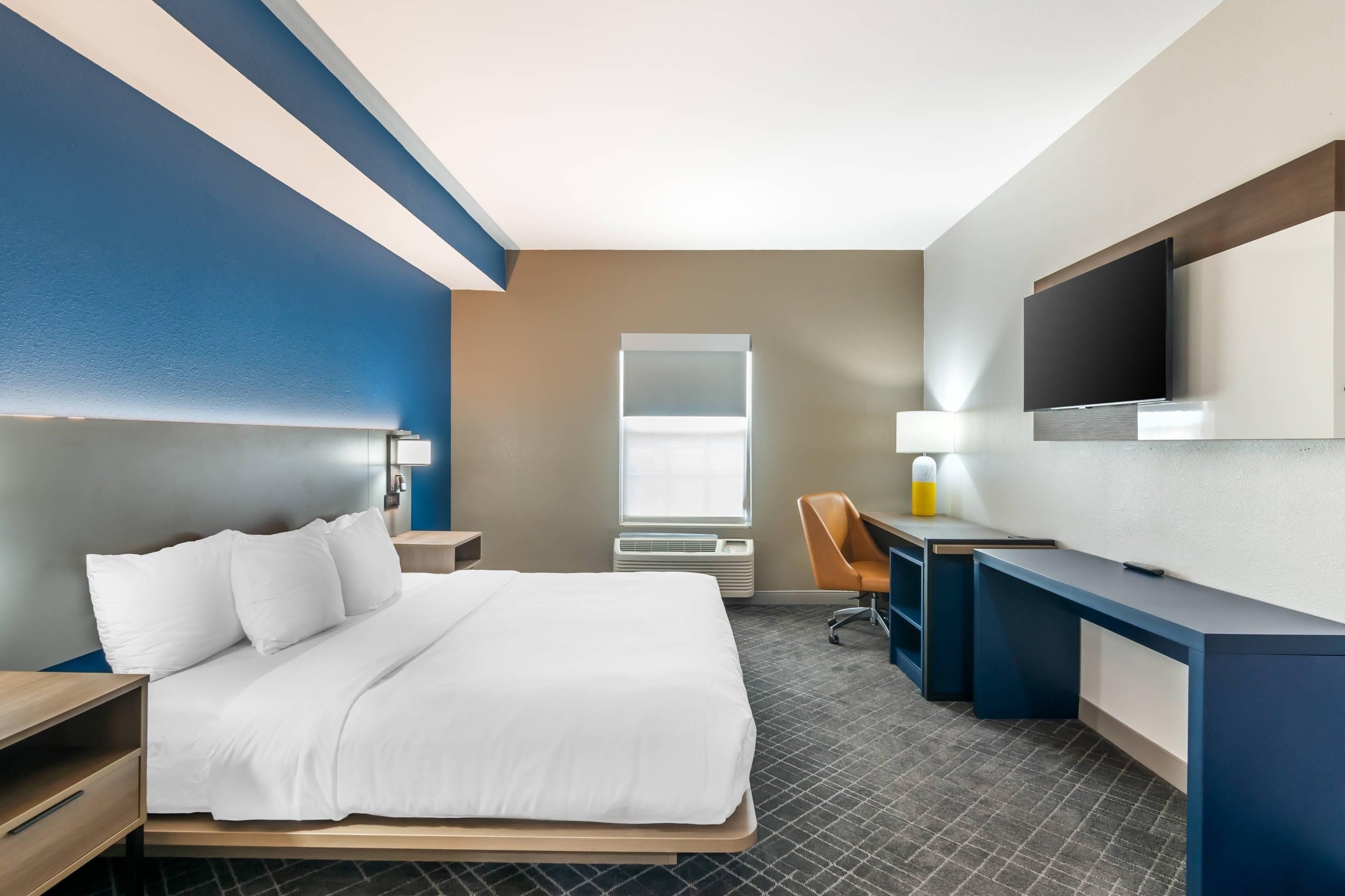 A hotel room with a bed, desk, chair, TV, and a window.