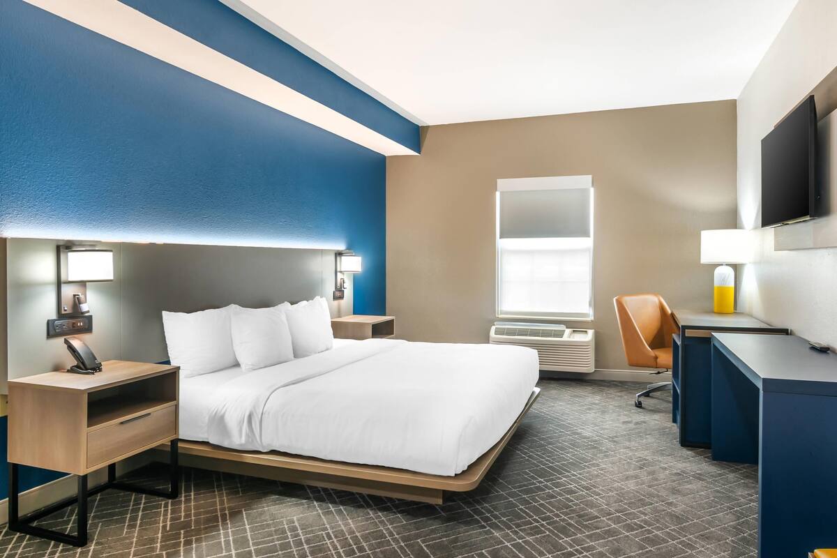 A hotel room with a bed, bedside tables, a desk, a chair, a TV, and a window.