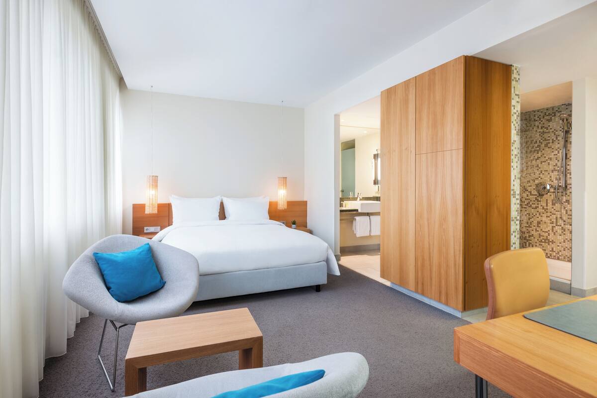 A hotel room with a bed, a desk, a chair, and a bathroom visible through an open door.