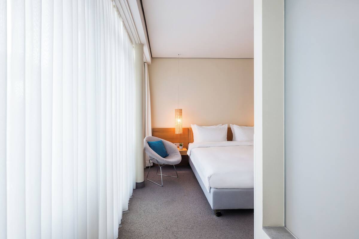 A hotel room with a bed, a chair, a nightstand, and a lamp.