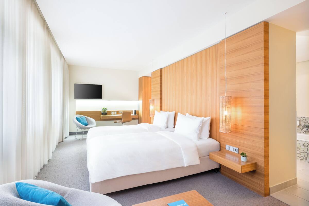 A modern hotel room with a large bed, a desk, a chair, and a TV.