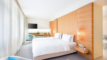 A modern hotel room with a large bed, a desk, a chair, and a TV.