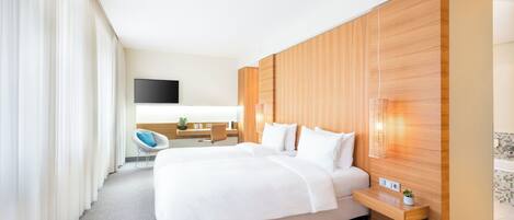 A modern hotel room with a large bed, a desk, a chair, and a TV.