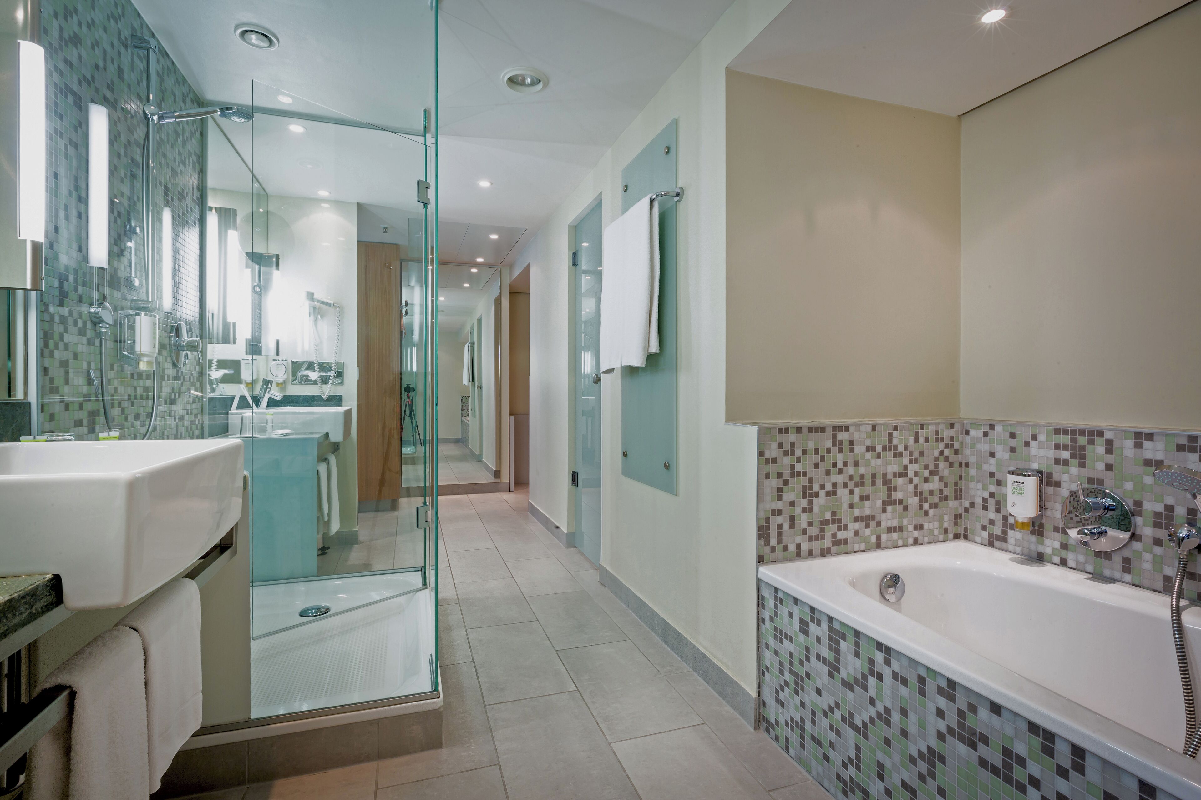 A modern bathroom with a glass shower enclosure, a large bathtub, and a tiled backsplash.