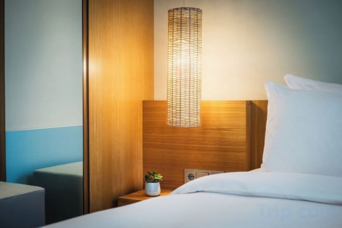 A hotel room with a bed, a nightstand with a lamp, and a small plant.