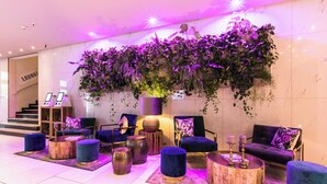 A modern lounge area with plush seating, round wooden tables, and a large wall-mounted plant display. - Lindner Hotel Berlin Ku’damm, part of JdV by Hyatt (Berlin)