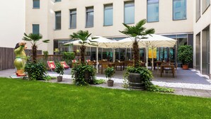A courtyard with outdoor seating, palm trees, and a building with multiple windows. - Lindner Hotel Berlin Ku’damm, part of JdV by Hyatt (Berlin)