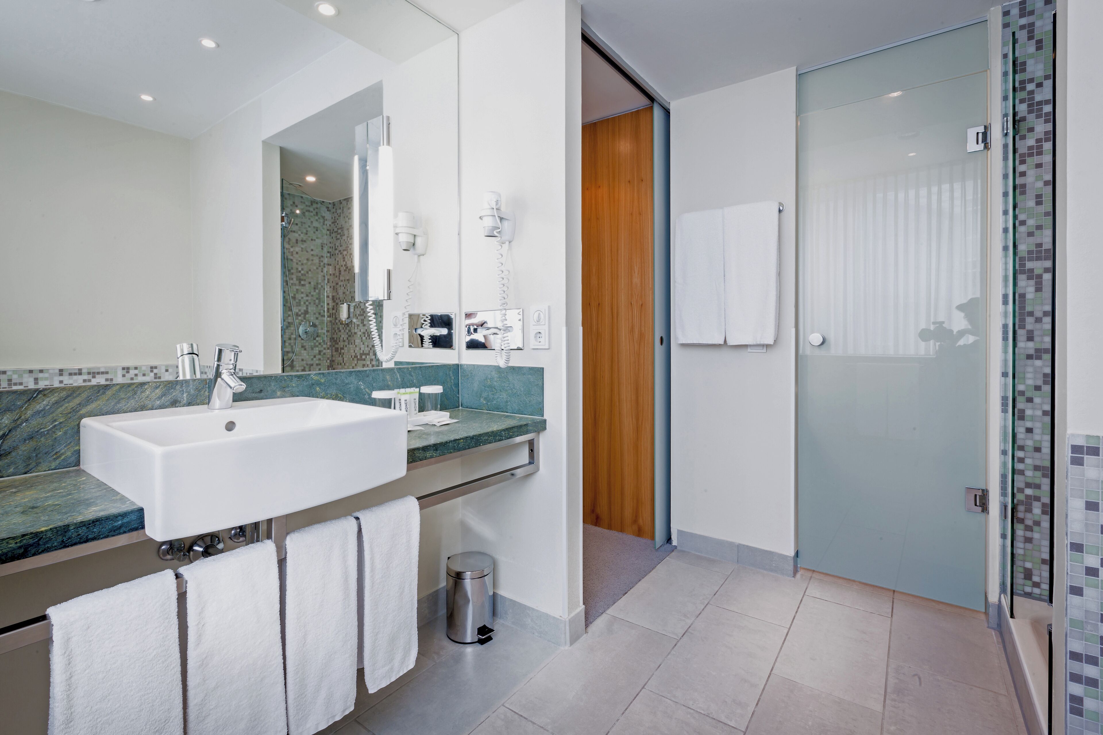 A modern bathroom with a large sink, mirror, and shower area.