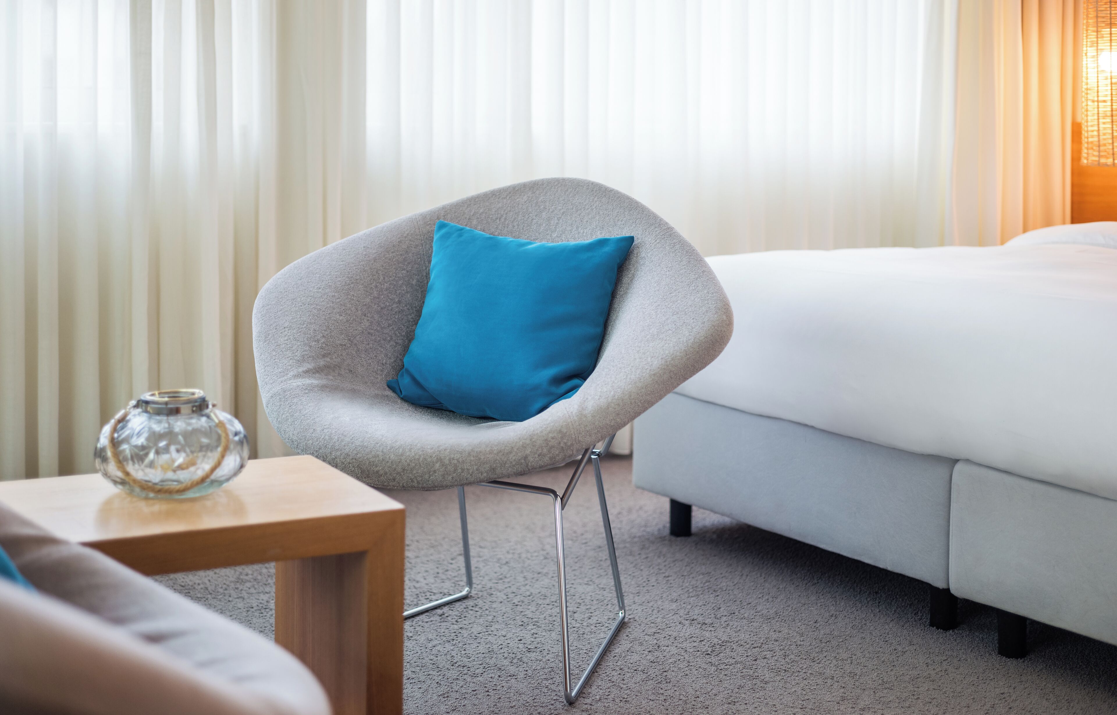 A modern hotel room with a grey armchair, a white sofa, and a bed.