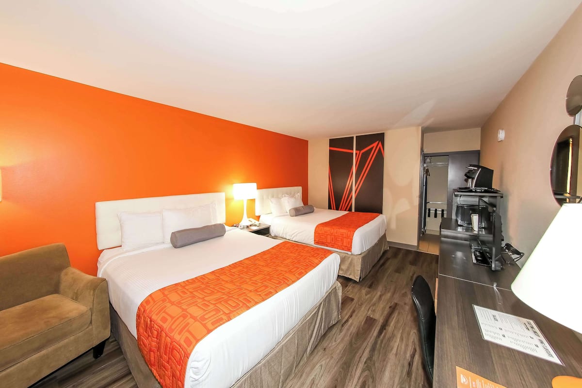 Quarto de hotel com duas camas, um sofá, uma escrivaninha e uma cozinha compacta.
