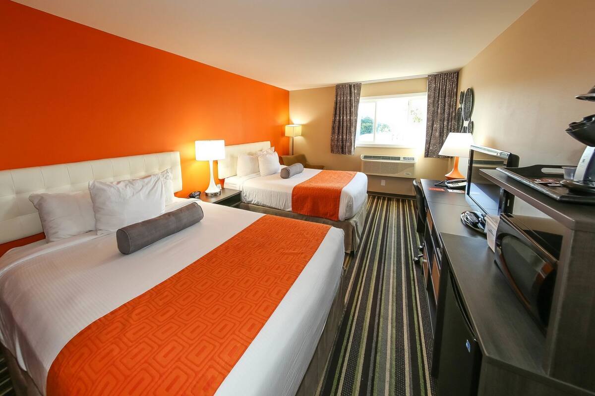 Quarto de hotel com duas camas, uma escrivaninha, televisão e janela com cortinas.