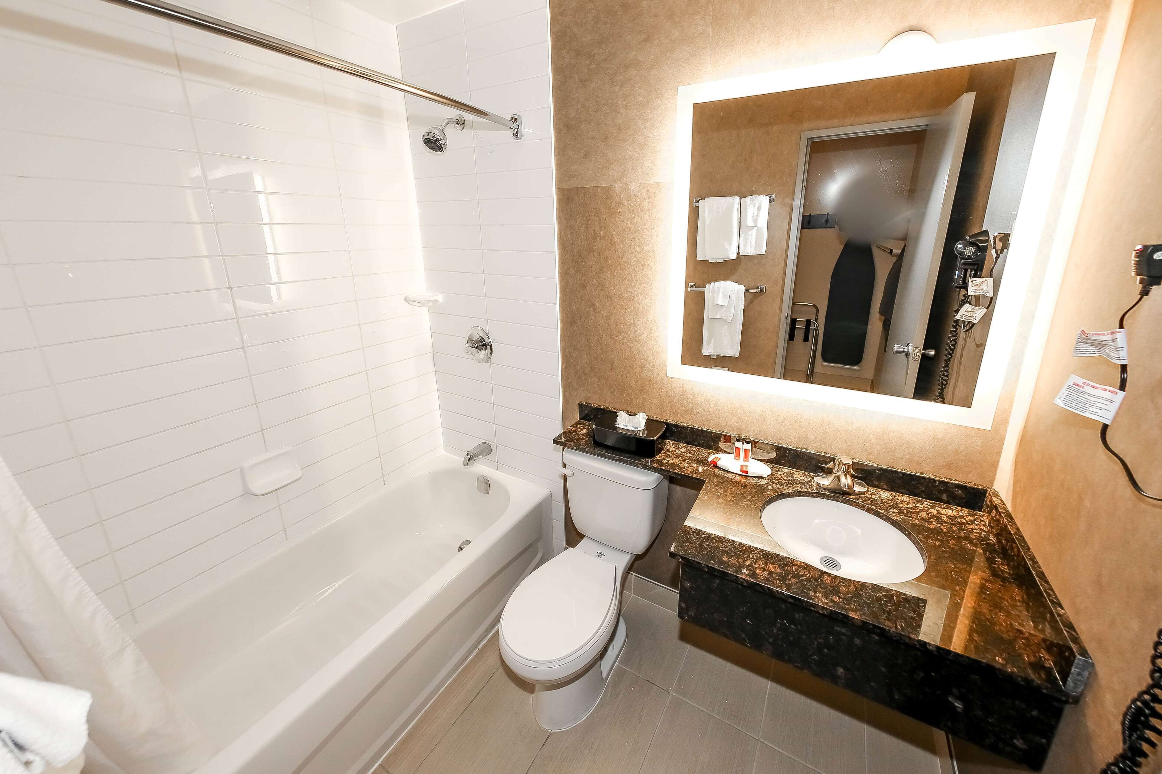 A bathroom with a bathtub, toilet, sink, and a mirror with a light above it.