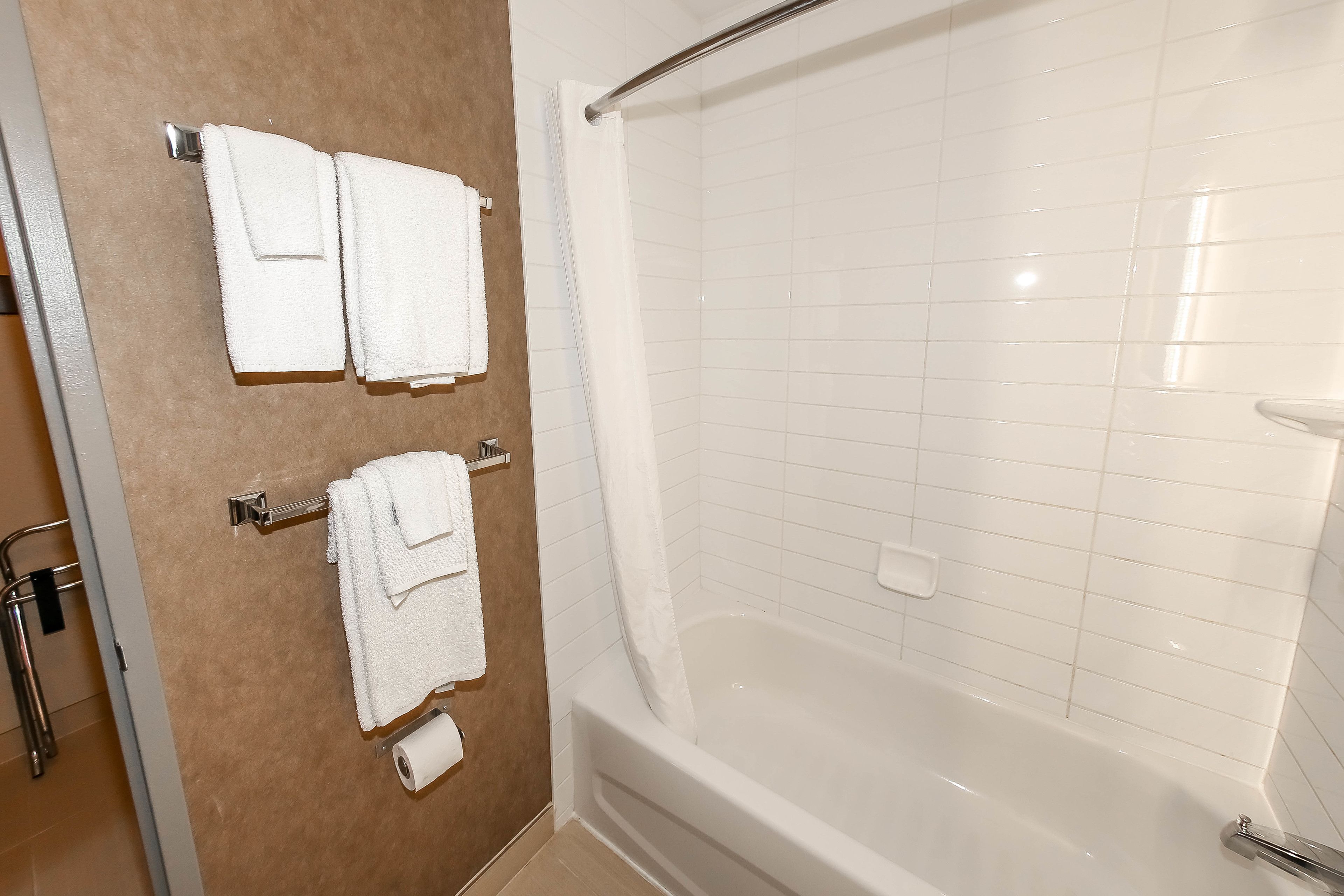A bathroom with a bathtub, white tiles, and two towels hanging on a rack.