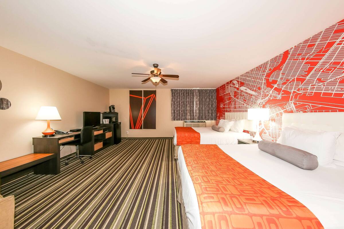 Quarto de hotel com cama, escrivaninha, cadeira e ventoinha no teto.